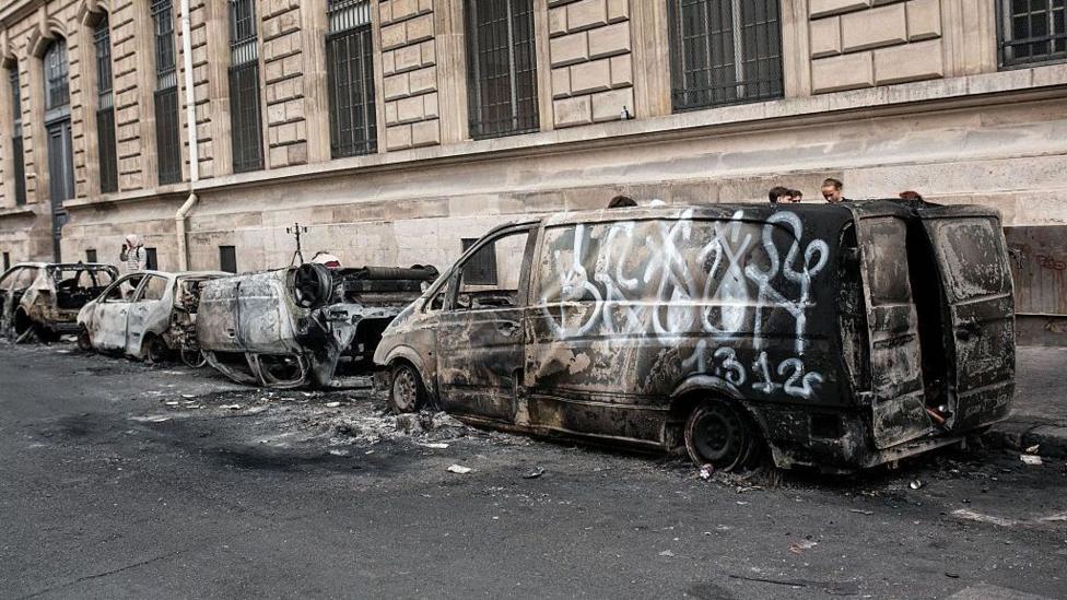 Several burned out vehicles, including one that is overturned, parked next to the pavement by a stone building in Paris on 19 October.