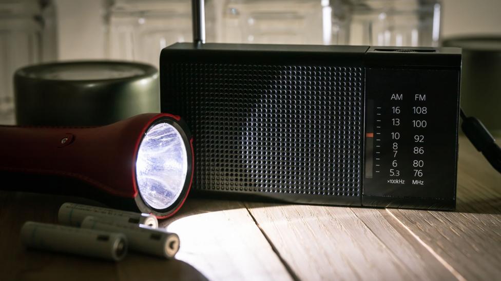 A red torch shines a beam of light on a black portable radio.