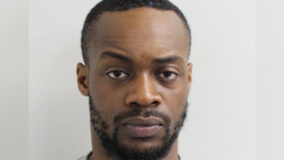 Gogoa Lois Tape, who has a small beard and very short hair, looks at the camera for a police custody photo.
