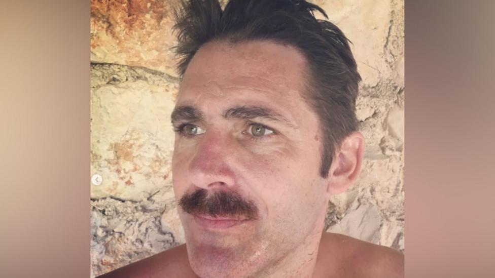 Paul Flack looks to the side in a selfie-style photograph he shared to Instagram, while sporting a moustache in front of a brick wall.