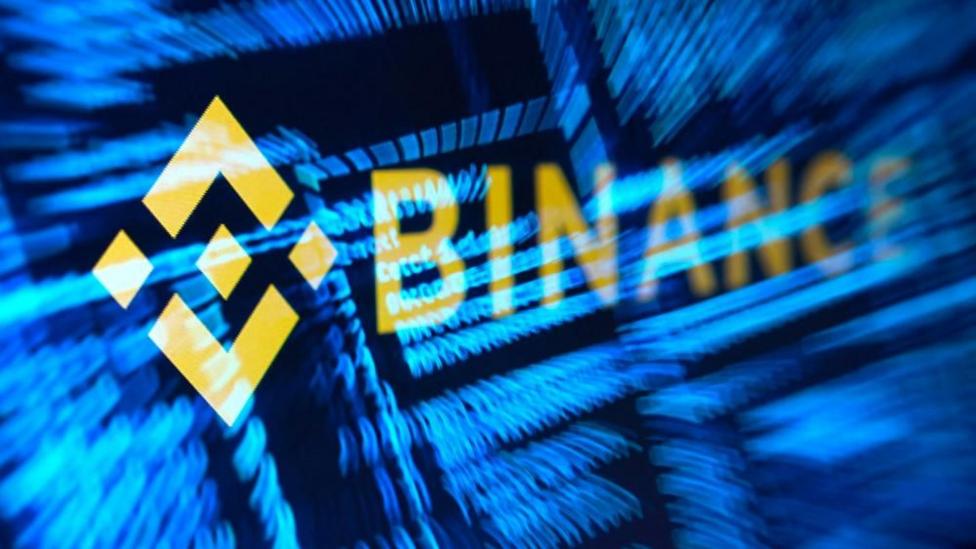 Жёлтый логотип Binance на фоне стилизованного синего хакерского кода