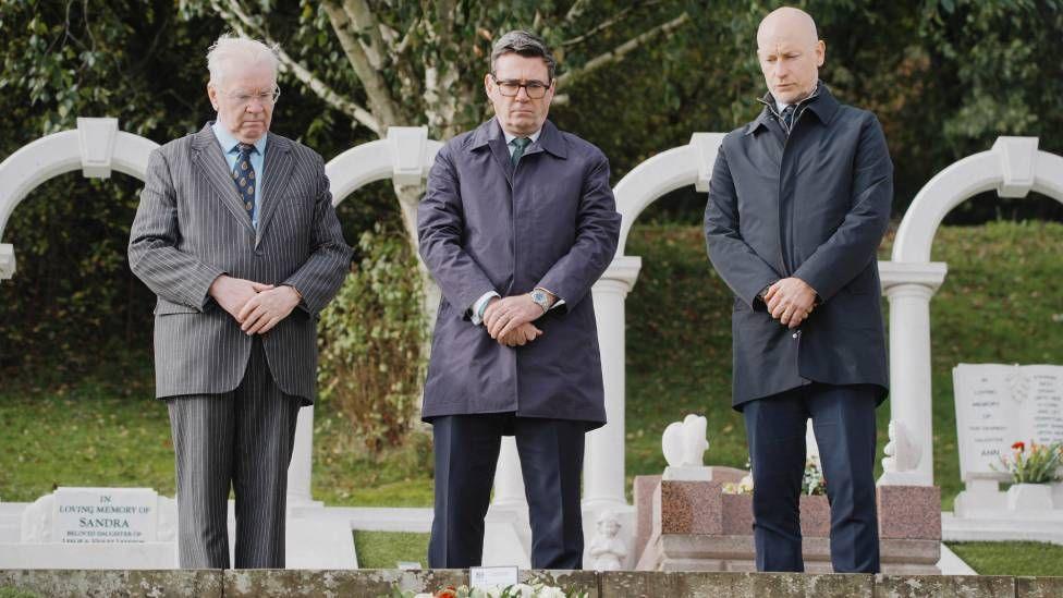 Three men in suits are seeing bowing and holding their hands in front of them