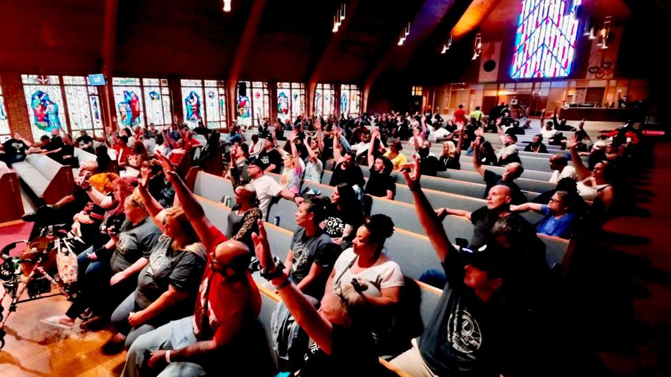 Members of the Hope Dealer Community, a recovery group, sit on rows of benches for a weekly meeting at Glenwood Church