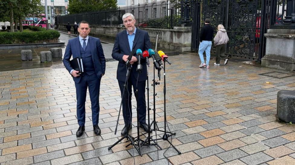 John O'Dowd va advokat mikrofon oldida turishgan