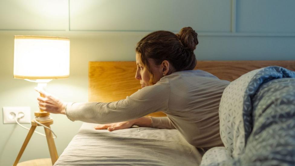 A woman reaches over to turn off a bedside lamp