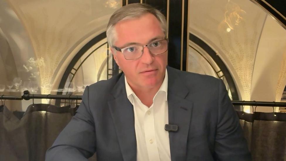 Yuriy Ryzhenkov, chief executive of Metinvest, being interviewed by the BBC. He is wearing a blue suit jacket and a white shirt. He has grey hair and is wearing glasses.