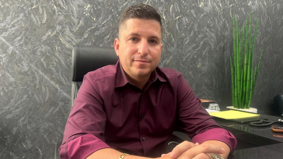 Ismael Labrador stoli oldida qöllarini çatiştirib ötirgan, töq qizil tugmali köylak kiygan