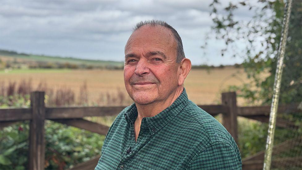 A portrait photo of Tony Chapman standing in his back garden near Corby in the Midlands. He is wearing a green shirt and looking straight at the camera.