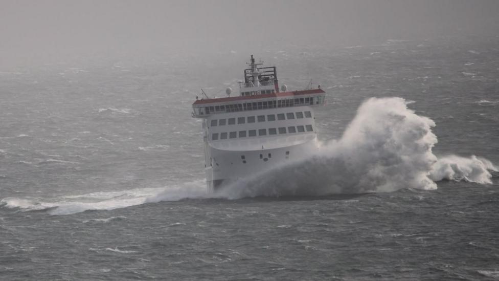 The Manxman ferry at sea on a choppy grey day with huge waves and white horses splashing to the right.