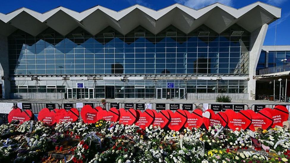 На фото — цветы и таблички в форме сердца с именами погибших, возложенные у вокзала во время собрания в первую годовщину трагедии на железнодорожном вокзале Нови-Сада, в Нови-Саде, 1 ноября 2025 года
