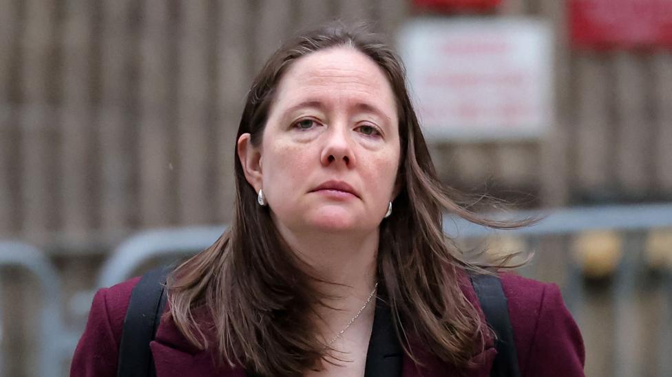 Maurene Comey wears a red jacket and has a blank expression