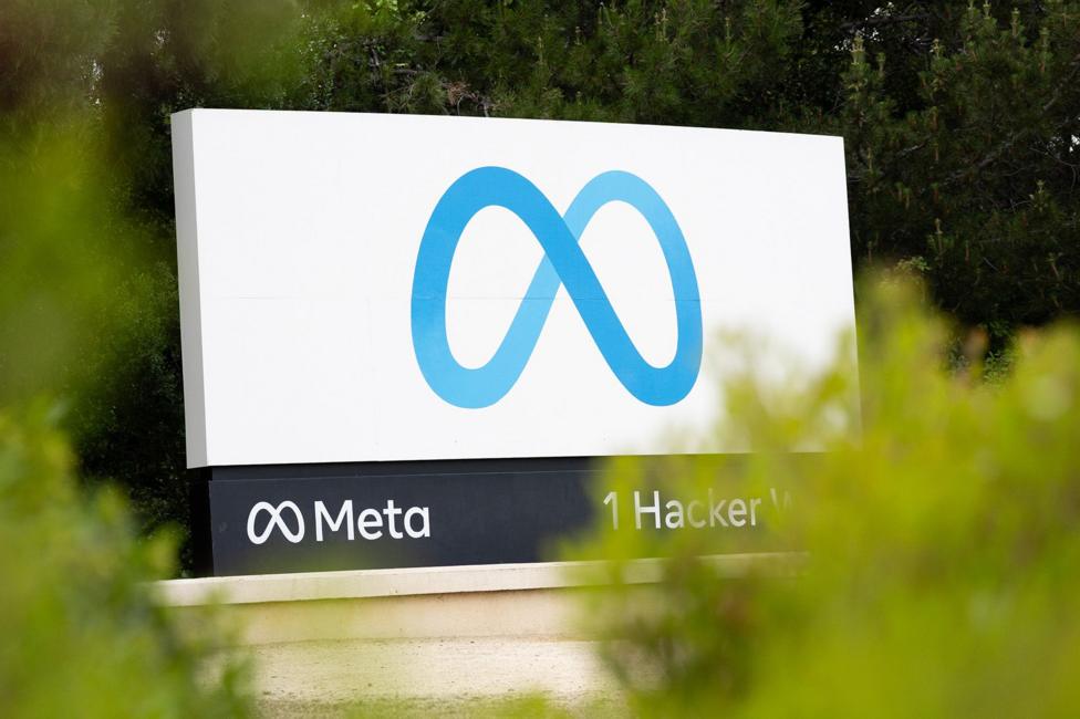 Meta's logo is seen on a sign reading 'Meta; 1 Hacker Way' with bokeh shrubbery in the foreground, pictured outside the Meta headquarters in California in April.