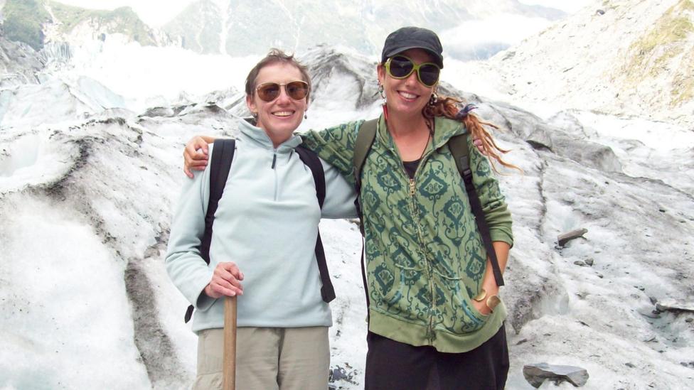 Kat and their mum at a glacier in New Zealand. Both are wearing sunglasses and are smiling. The glacier is covered in snow.
