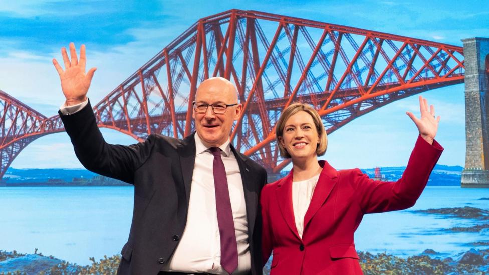 Scottish First Minister and SNP party leader John Swinney with Deputy First Minister Jenny Gilruth wave to delegates on stage at the SNP annual conference.