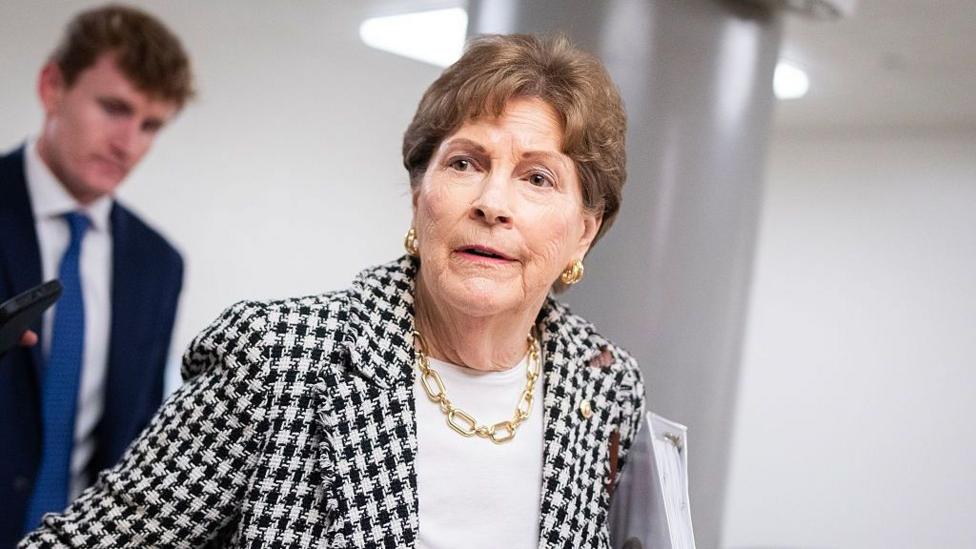 Sen. Jeanne Shaheen, who has short brown hair and is wearing a blazer with a black and white dogtooth pattern, a white top and gold jewellery, talks with reporters during votes in the US Capitol on Wednesday, September 30, 2026.