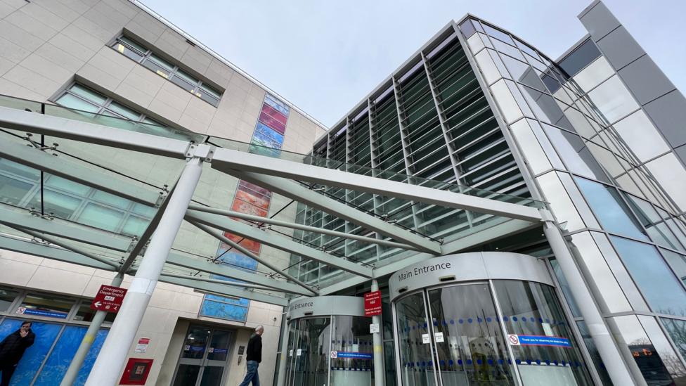 The entrance to Broomfield Hospital. It has several storeys and has a mostly silver facade.