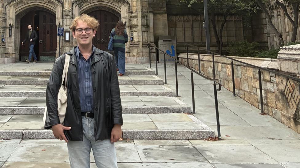 Charlie West standing in front of steps leading up to an old building. He is wearing a leather jacket and pale jeans