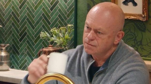Ross Kemp looking annoyed while drinking a cup of tea