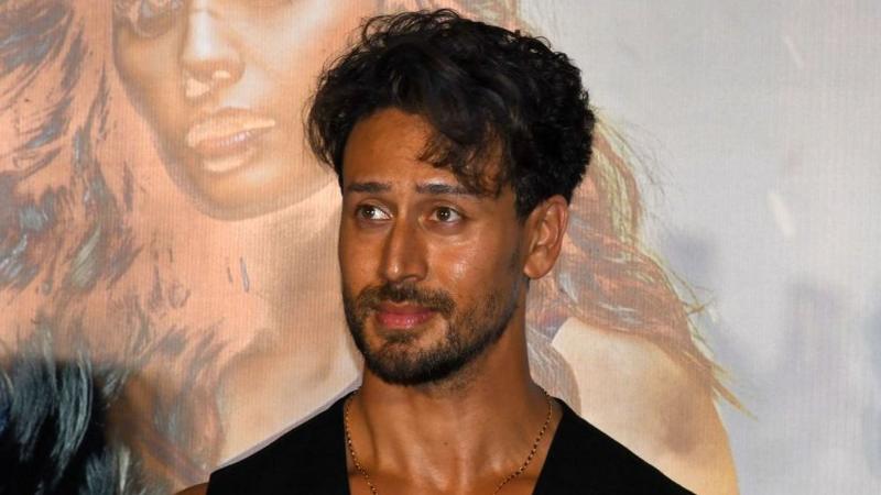 Bollywood actor Tiger Shroff at an event, wearing a black vest and necklace.