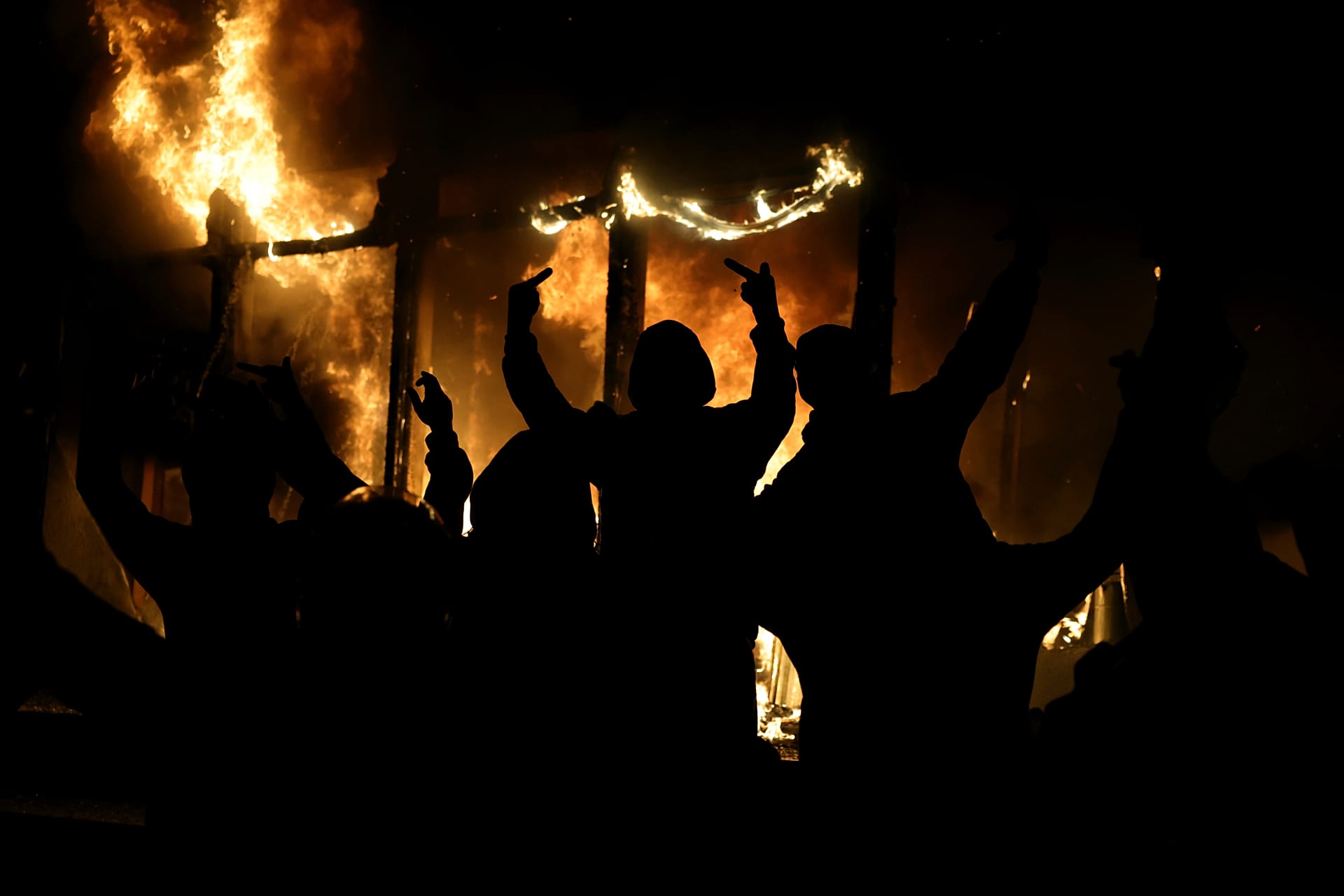 A hooded protester raises his middle fingers as fire engulfs the Justice Ministry during a violent escalation of anti-government unrest in Tirana, Albania, Wednesday, 14 Oct.