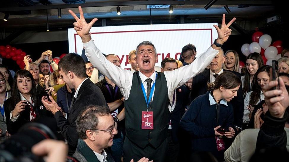 A man in a waistcoat with grey hair celebrates