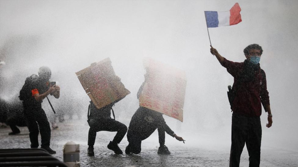 A masked protester holds a French flag as French police use a water canon amid clashes during a demonstration by French high school and university students in Paris.
