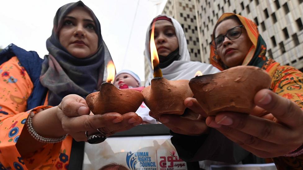 Three women at a vigil for the 14 newborns holding up candles