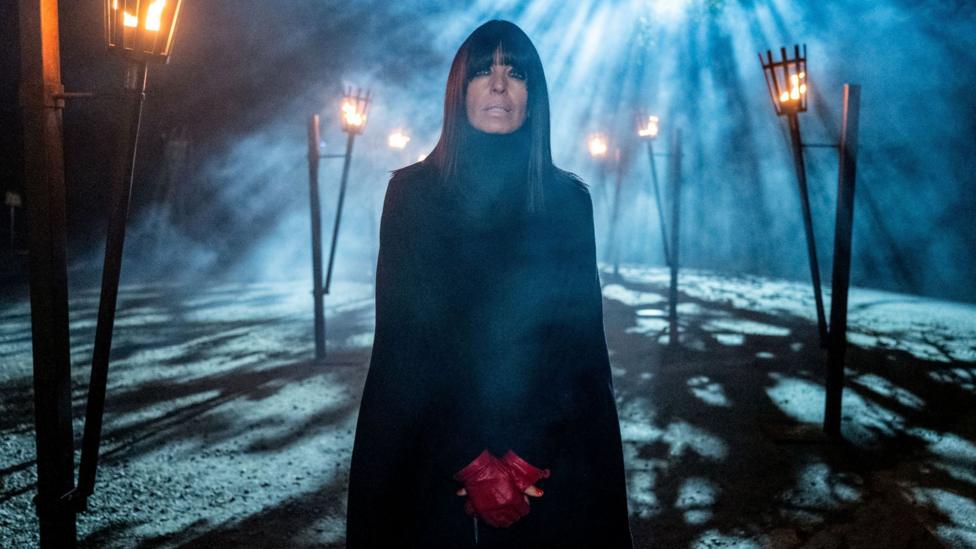 Promo shot for The Traitors with Claudia Winkleman wearing all black apart from red fingerless gloves 