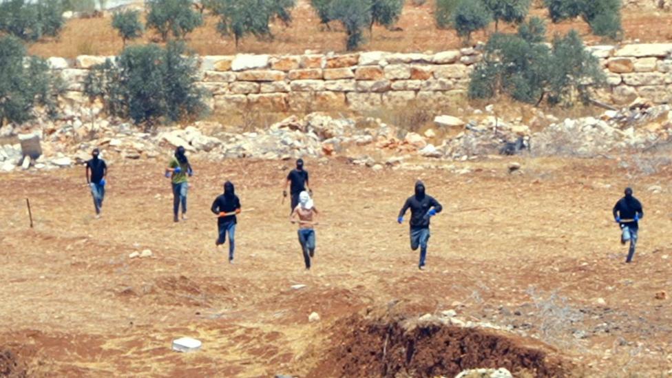 Seven masked figures run across a stretch of orange terrain towards the camera
