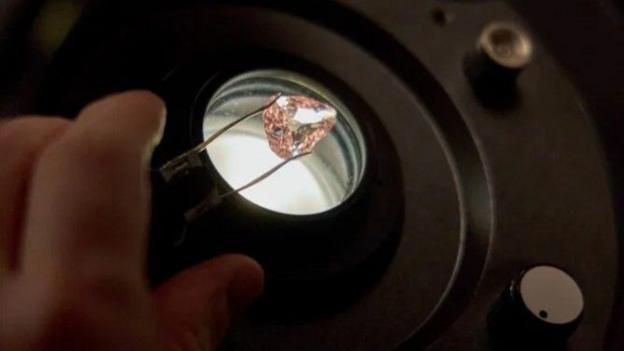 A person inspects the backlit Grand Condé diamond under a microscope.