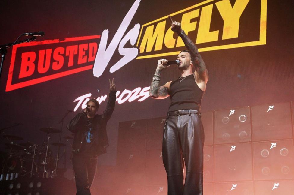 Charlie Simpson and Matt Willis from Busted standing in front of a screen that reads 'Busted VS McFly Tour 2025'
