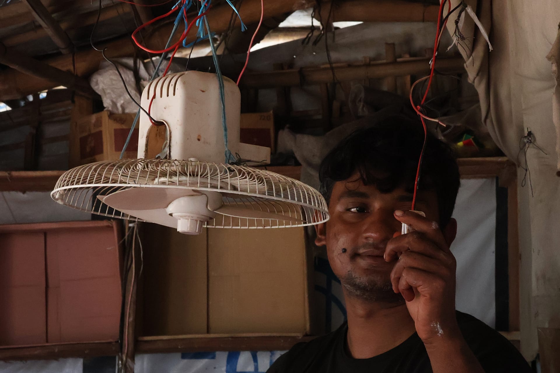 In this photo taken with a phone, Mohammed Hares turns on a solar-powered fan inside his shop Oct. 4, 2026, in Teknaf, Bangaldesh.