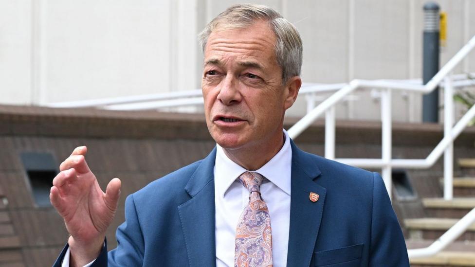 Nigel Farage, in a suit and tie, makes a point with his hand