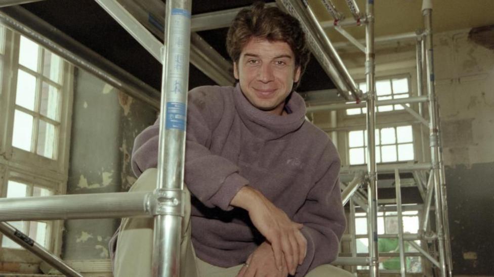 A young Nick Knowles posing perched on scaffolding inside a mid-renovation property