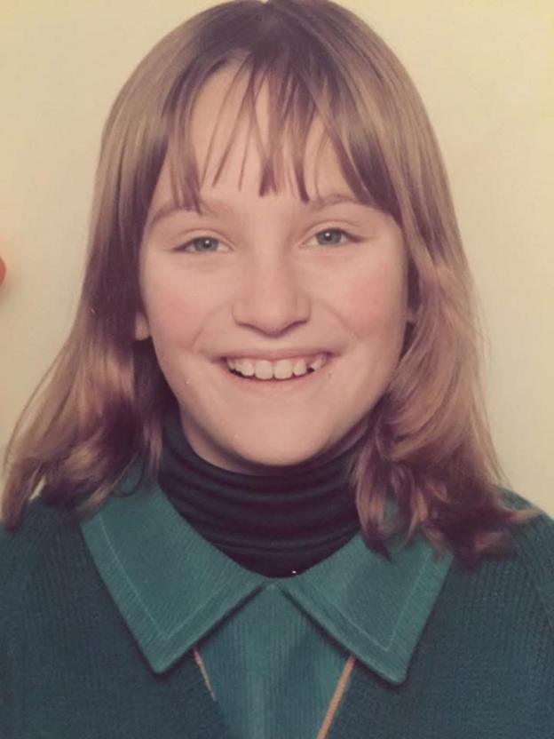 Студийный портрет Рэйчел в детстве, изображённой по плечи на светлом однотонном фоне. У Рэйчел волосы до плеч с чёлкой, она смотрит прямо в камеру и улыбается. На ней тёмная одежда с воротником-стойкой под бирюзово-зелёный джемпер с воротником.
