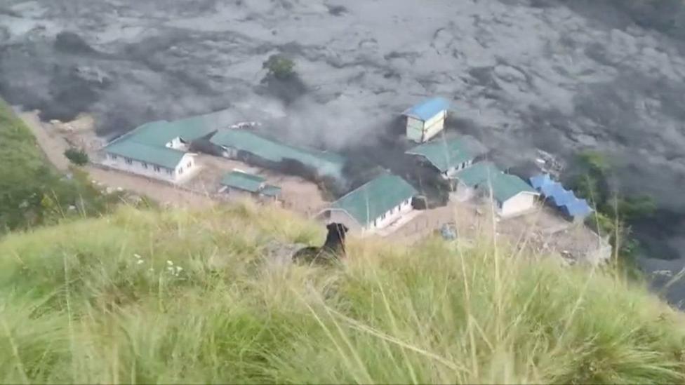 A building complex with green roofs is swamped with black flood water.