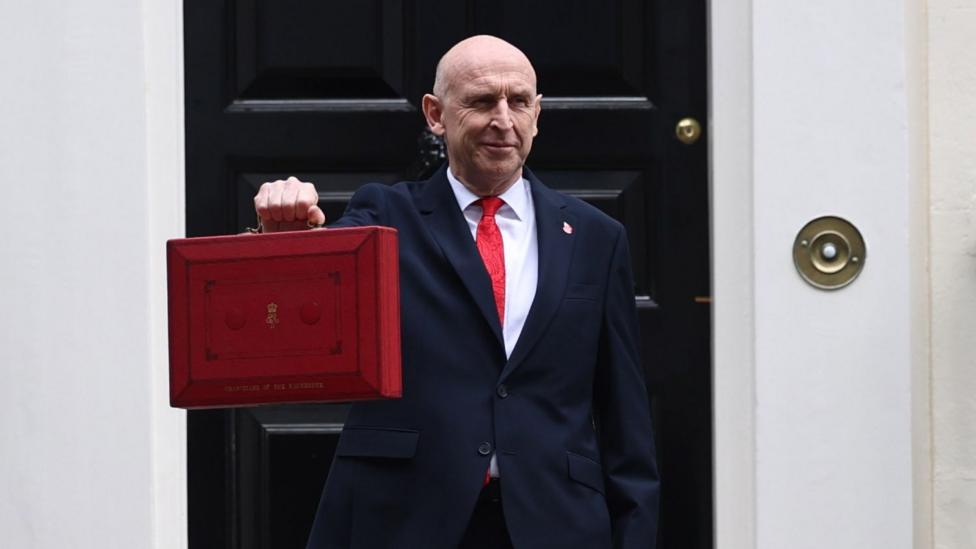 John Healey 11 Downing Street oldida eskirgan qizil portfel — redboxni ushlab turibdi.