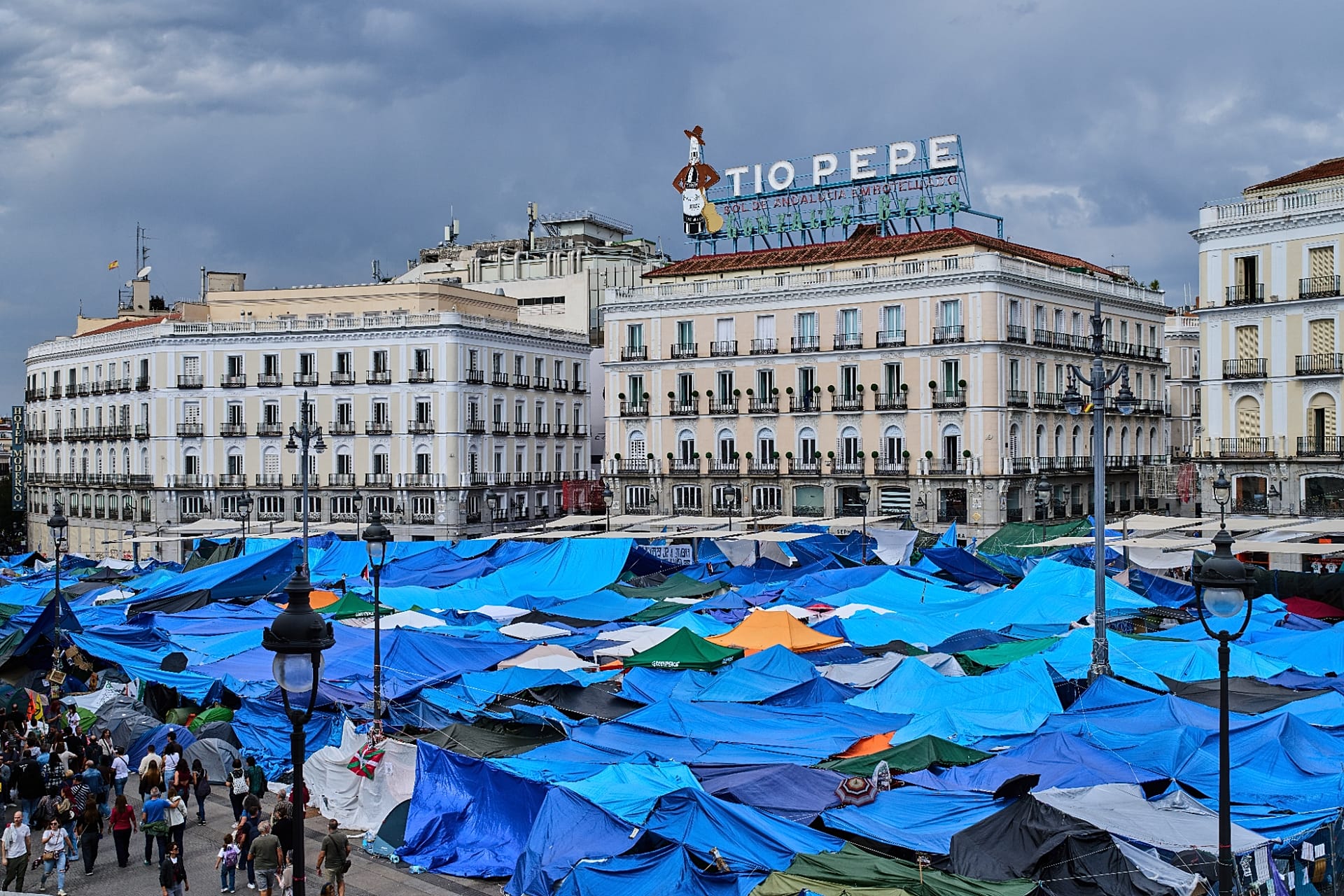 FILE. People walk among tents set up by protesters at the Puerta del Sol square demanding stronger laws to protect renters in Madrid, Spain, 17 Oct. 2026