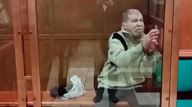 Стивен Хаббард, пожилой мужчина в светло-зелёном джемпере, сидит в наручниках в стеклянном боксе в зале суда.