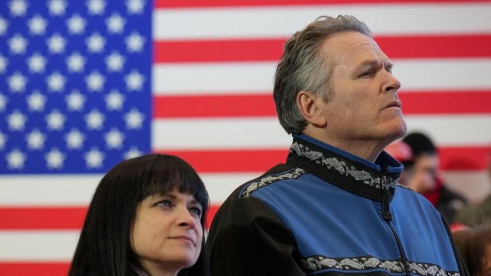 File image of Governor Mike Dunleavy standing in front of a US flag at an event