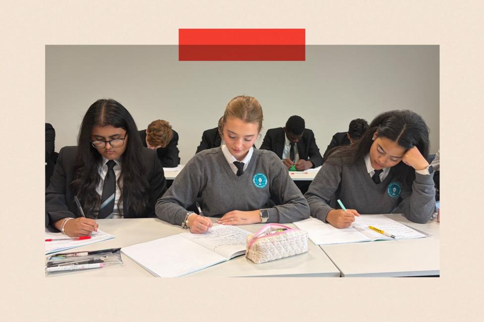 Three teenage female students sat at desks studying. The one on the left is wearing a dark blazer and the other two a grey jumper over their shirt and tie