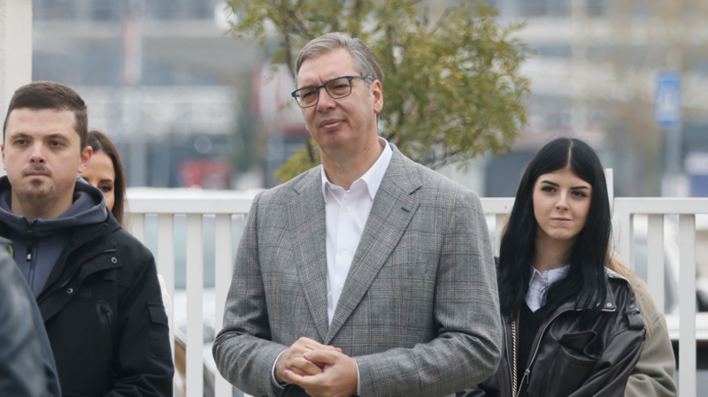 Aleksandar Vucic in a grey suit and white shirt waits in a polling station queue