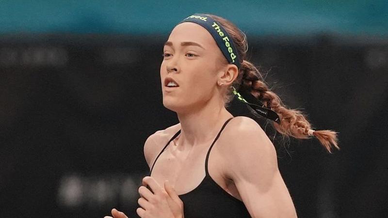 Joanna Wietrzyk qora sport brauzeri va 'the feed' sözlari yaşil harflar bilan bosilgan töqsiyoh tasma taqqan. Soçi örilgan, u yuguriş jarayonida.