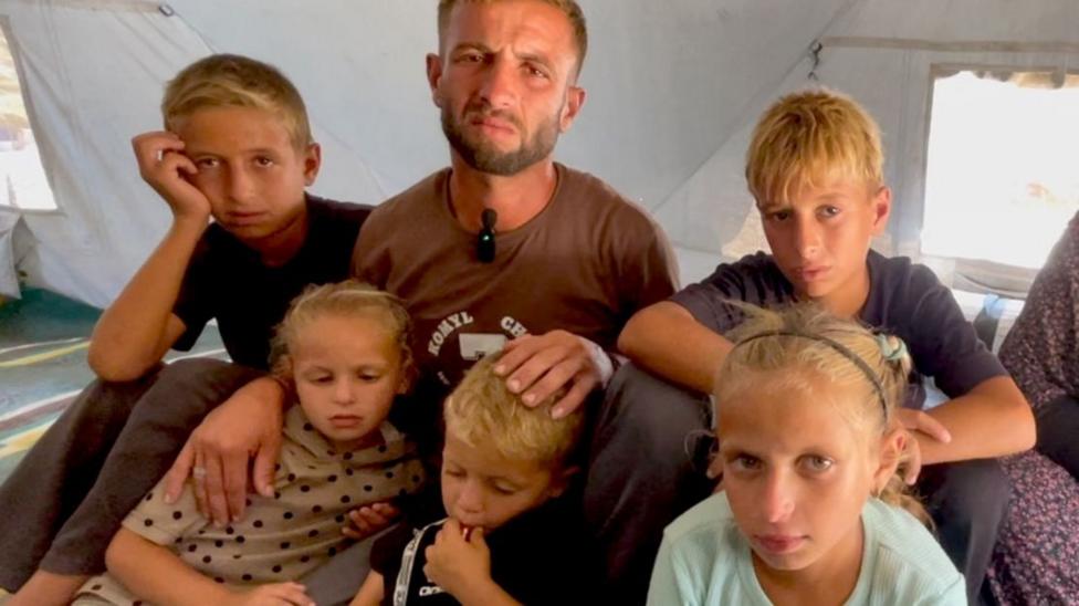 Мужчина лет тридцати сидит с пятью детьми — двумя девочками и тремя мальчиками — внутри палатки