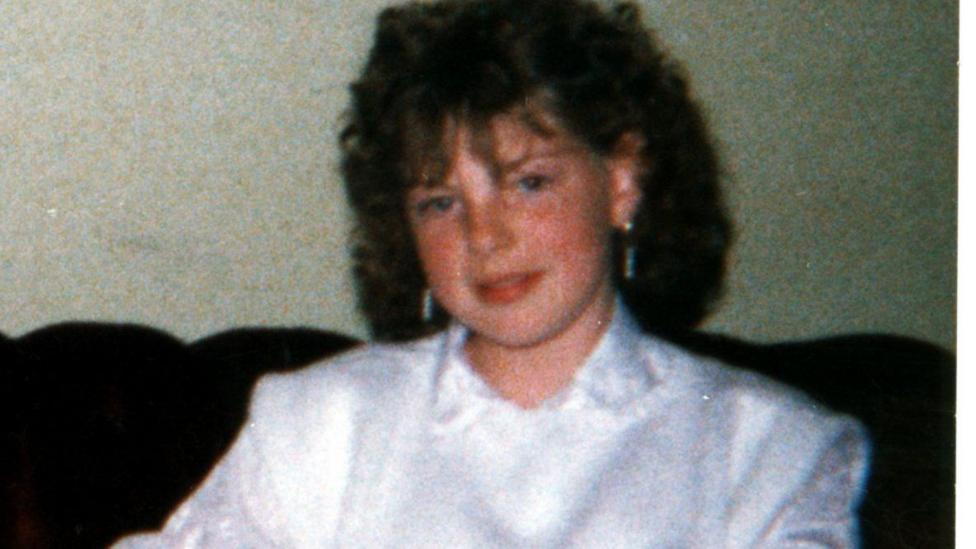 Old colour photograph of Diane Watson with curly hair wearing a white jacket and blouse, seated on a sofa indoors and facing the camera.
