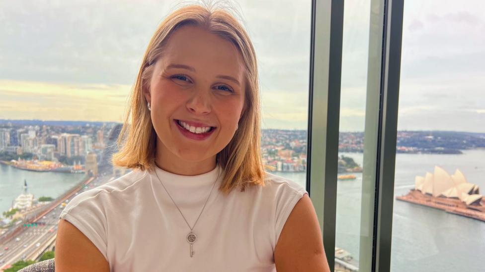 Rachel James stands in front of a window that looks over Sydney harbour and the Australian city's famous opera house