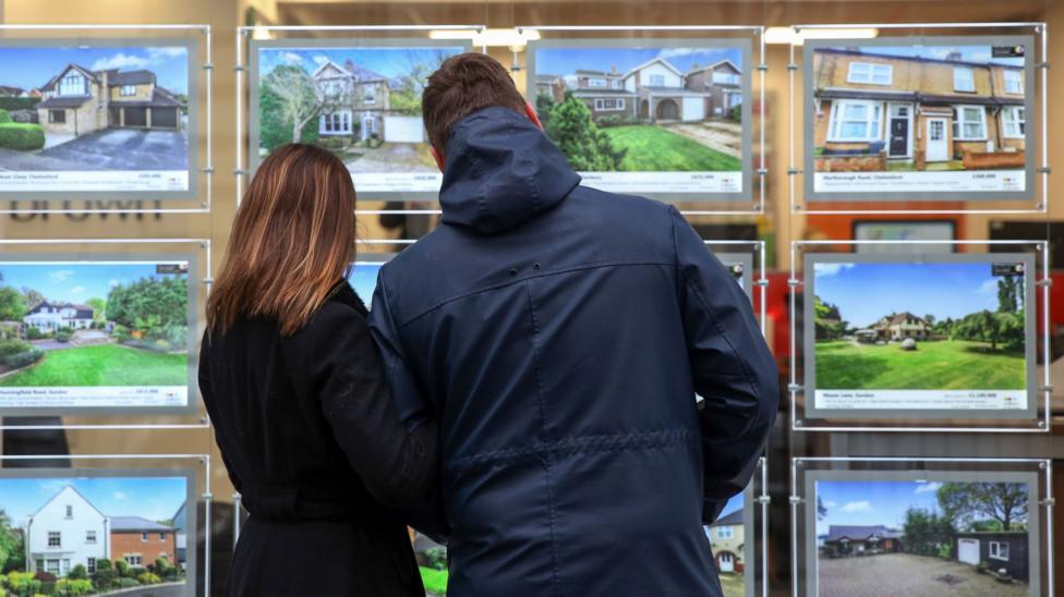 A couple look at houses for sale in the window of an estate agent