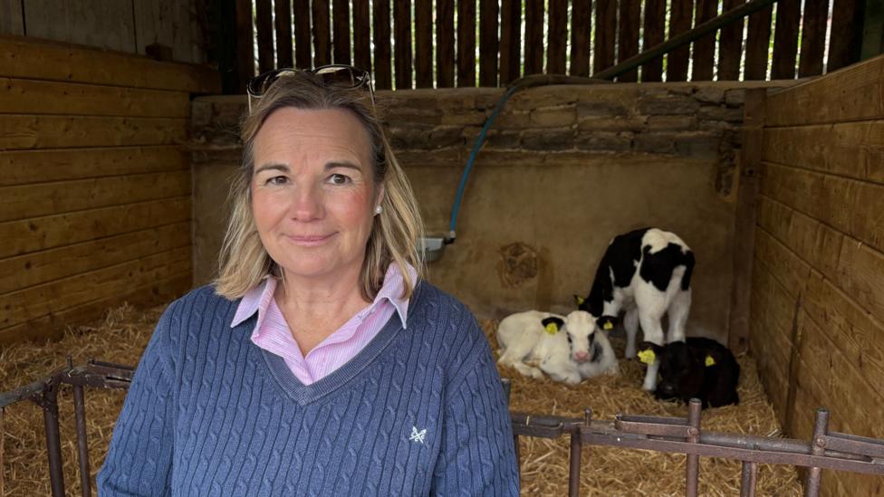 Sally Phillips standing in front of a barn with three calves resting on straw bedding.
