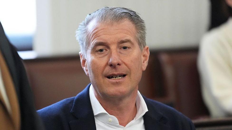 Co-plaintiff Stephan Hensel, former husband of defendant Christina Block and father of their children, looks at the camera - with combed back grey hair, a white collared shirt and blue jacket
