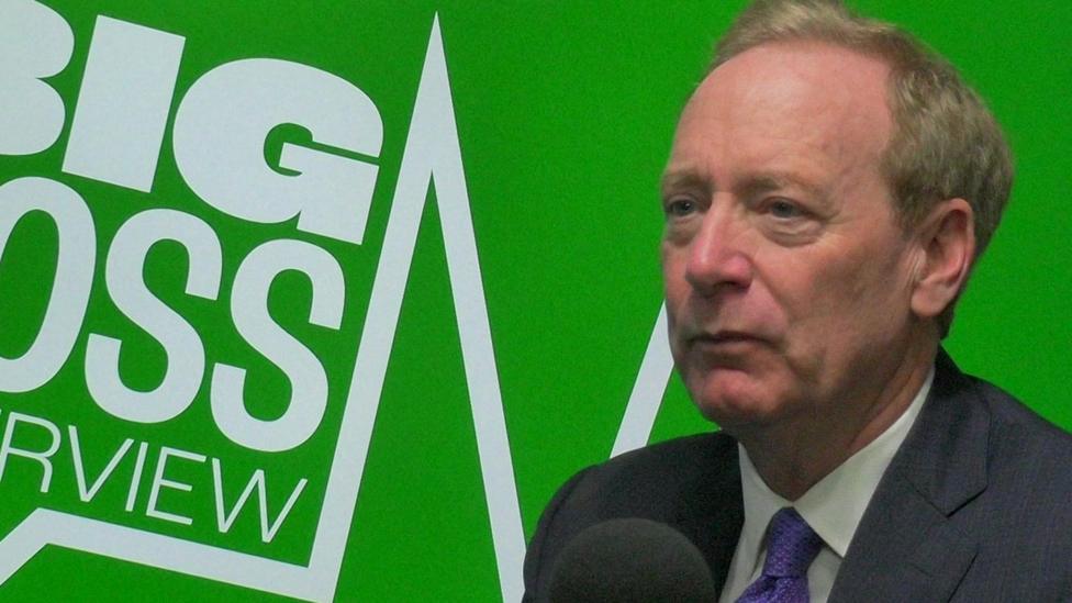 Microsoft president Brad Smith sitting in front of a microphone in a radio studio with Big Boss Interview written on a green background behind him